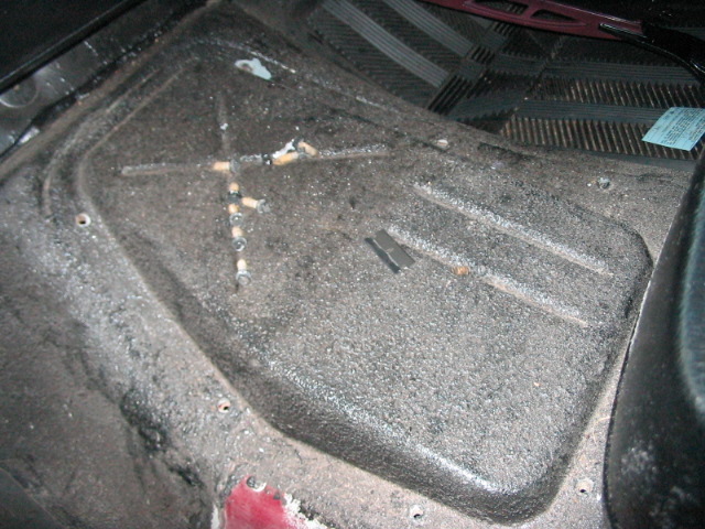 Interior floor of a vehicle, showing a textured surface with some debris and cigarette butts