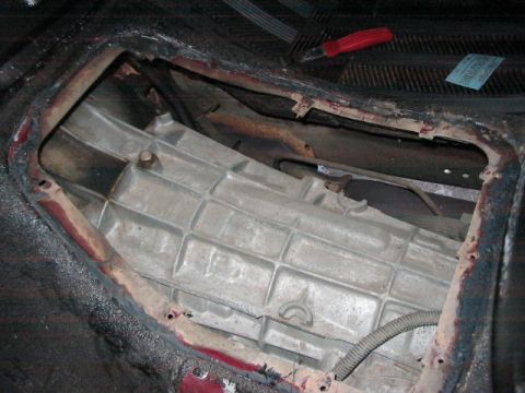 1991 Ford Bronco - The transmission tunnel of a vehicle is exposed, revealing the transmission casing and surrounding components. A tool rests on the dashboar…