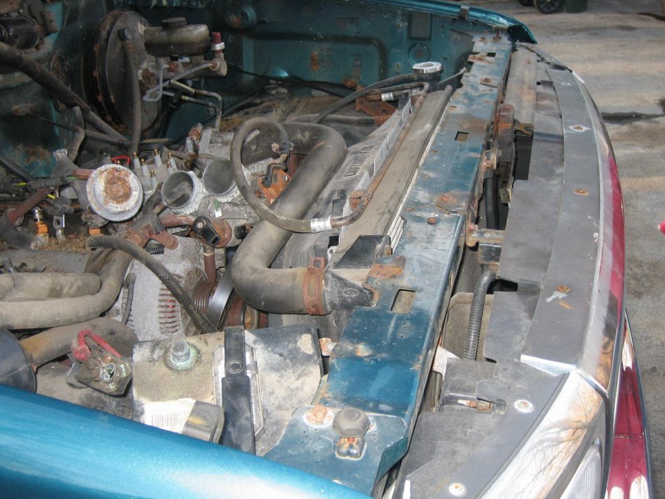 Engine bay showing radiator, hoses, and alternator. Some rust is visible on components
