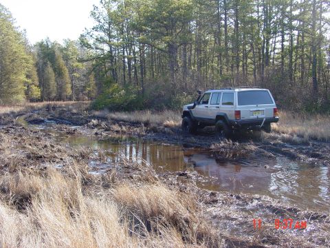 1995 Dodge 1500 - A silver Jeep Cherokee XJ tackles a challenging muddy off-road course, demonstrating its 4x4 capabilities.