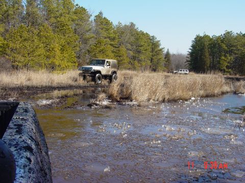 1995 Dodge 1500 - Two off-road vehicles navigate a muddy terrain with trees and dry grass.