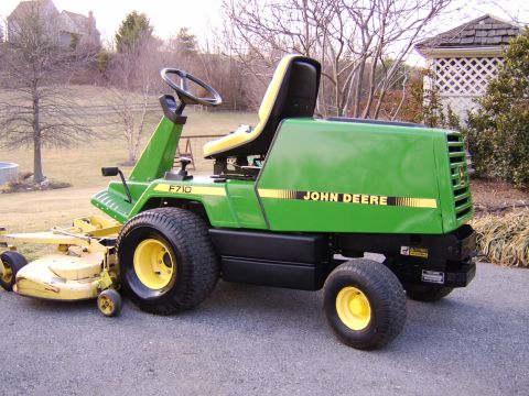 1996 Mercury Grand Marquis - A green John Deere F710 riding mower is parked on a paved surface in front of a house and trees.