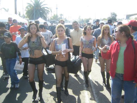1990 Ford Bronco - Four young women in matching cropped tops, shorts and boots walk through a sunny outdoor event crowd.