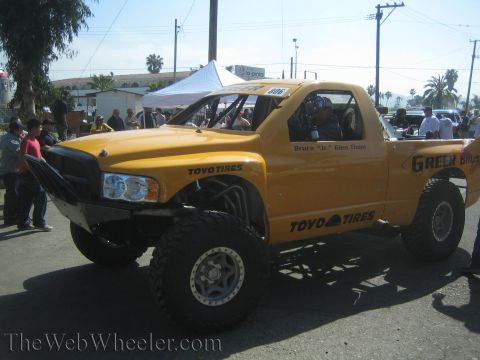 1990 Ford Bronco - yellow number 806 Greer Bros / Toyo Tires off-road race truck with a Dodge-style front end parked on a sunny lot with spectators.