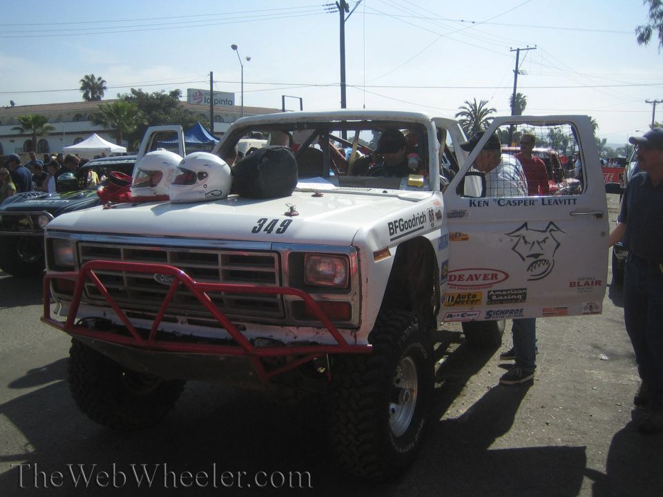 White off-road race truck 349 with two helmets on hood and red front bumper in a crowd