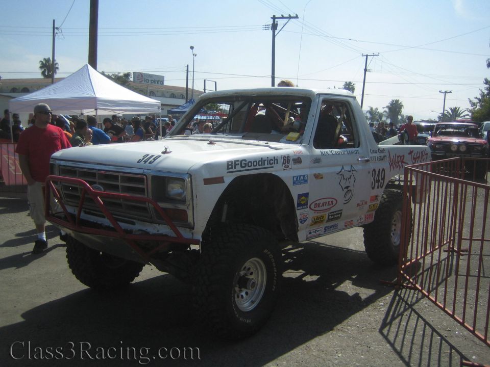 Lifted white Ford race truck 349 on large tires behind a barrier at an event
