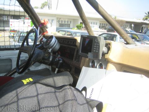 1990 Ford Bronco - Cockpit of an off-road race truck with a tan dash, aftermarket gauges, a Lowrance GPS unit, roll cage and a quick-release steering wheel.