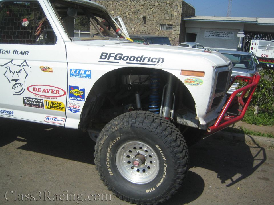 Front fender and BFGoodrich tire of a white off-road truck with red bumper and blue coilover