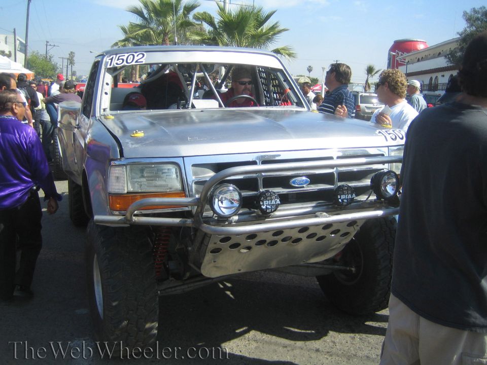 Silver Ford off-road race truck 1502 with chrome bumper and light bar in a crowd