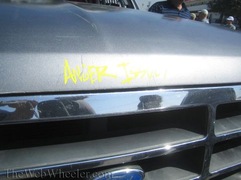 1990 Ford Bronco - Close-up of a silver Ford hood and chrome grille hand-painted with the words 'Anger Issues' in yellow marker.