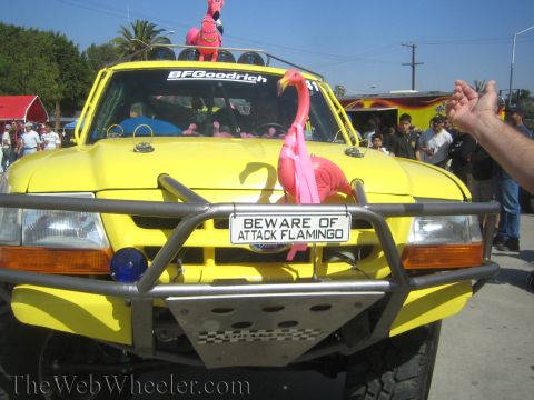1990 Ford Bronco - Front of a yellow off-road race truck decorated with pink flamingos and a license plate reading 'BEWARE OF ATTACK FLAMINGO.'