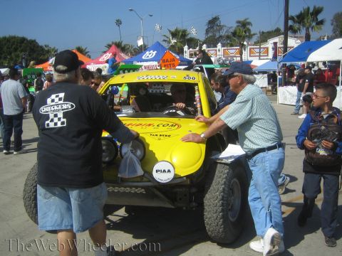 1990 Ford Bronco - yellow open-cockpit off-road race buggy numbered 500 is surrounded by spectators amid colorful canopies at a busy pit area.