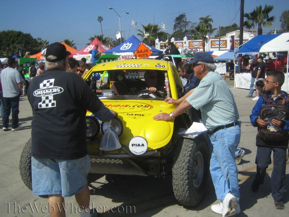 Yellow off-road race buggy 500 surrounded by spectators at a busy pit area