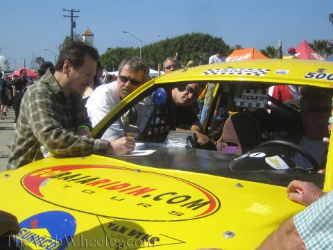 1990 Ford Bronco - Two men lean over the hood of yellow off-road race buggy 500, signing paperwork during contingency at a sunny outdoor event.