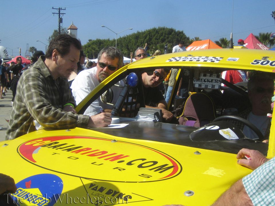 Men signing paperwork on the hood of a yellow off-road race buggy 500 outdoors
