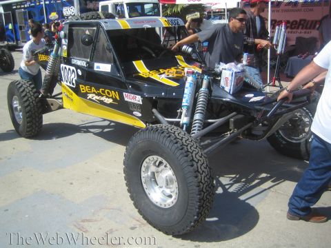 1990 Ford Bronco - yellow and black tube-frame off-road buggy lettered Beacon Racing sits among crew and spectators at an outdoor event.