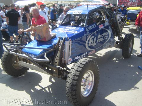 1990 Ford Bronco - blue single-seat off-road race buggy with F&L Racing Fuel graphics is parked in a dense crowd at an outdoor event.