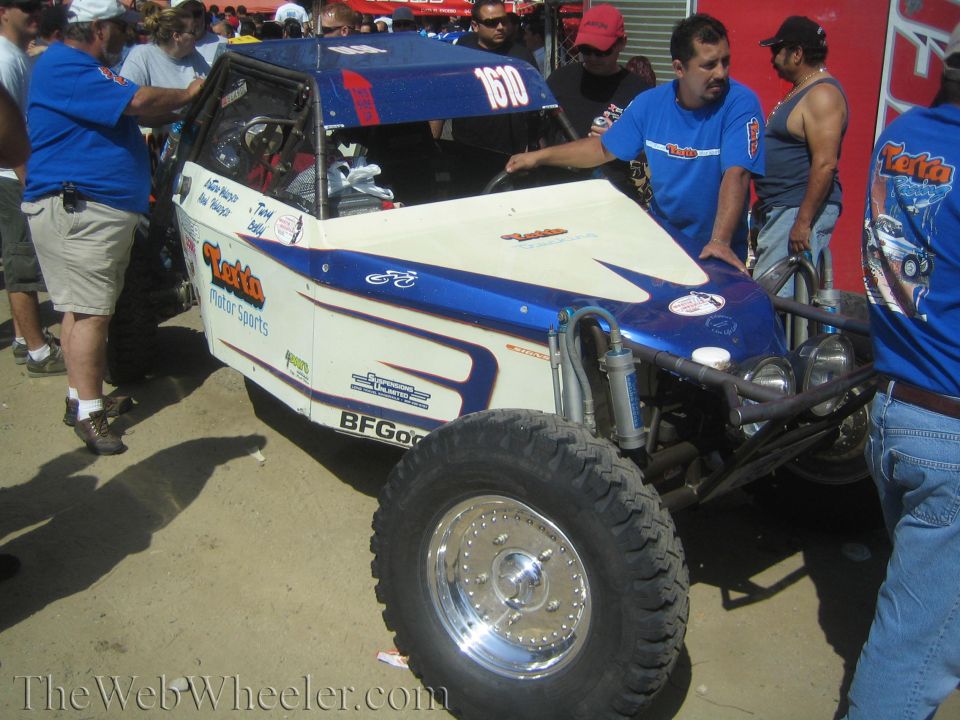 Blue and white off-road buggy being inspected by crew in blue shirts