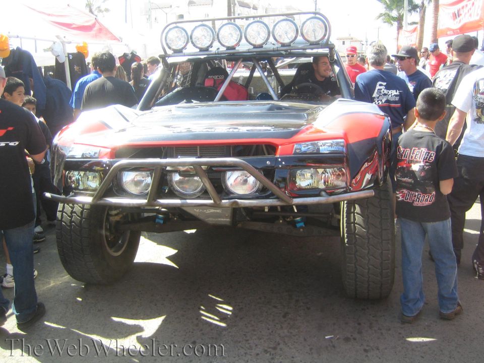 Front of red and black off-road race truck with roof light bar in a crowd