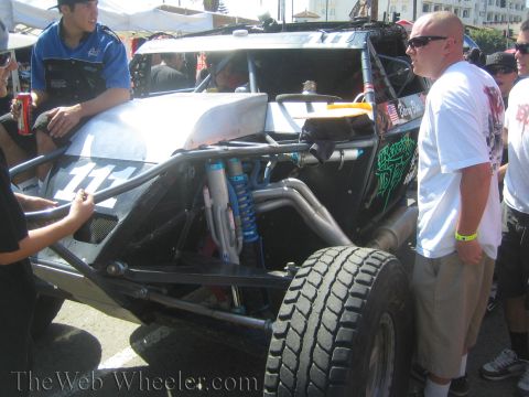 1990 Ford Bronco - black tube-frame off-road race buggy marked 111 is parked among spectators in bright sunlight at an outdoor event.