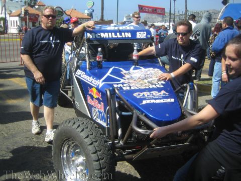 1990 Ford Bronco - People push a blue off-road race buggy with McMillin and Red Bull graphics, numbered 1602, through a crowd at an outdoor event.