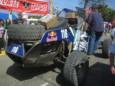 1990 Ford Bronco - rear of a blue off-road race buggy numbered 116 shows a Red Bull logo and mounted spare tire beneath a Tecate banner.
