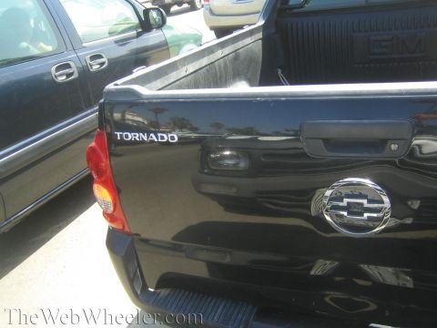 1990 Ford Bronco - Close-up of a black pickup tailgate showing a chrome Chevrolet bowtie emblem and a TORNADO nameplate.