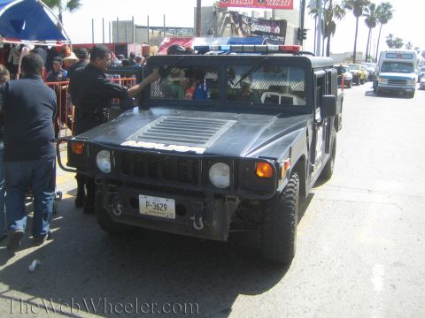1990 Ford Bronco - front of a black H1-style Hummer with a roof light bar and plate P-3629 is surrounded by people on a busy street.