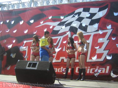 1990 Ford Bronco - group of women in red outfits and a man in a yellow shirt stand on a stage in front of a large checkered-flag Tecate banner.