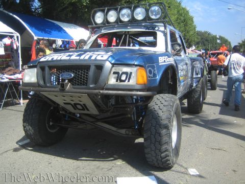 1990 Ford Bronco - blue Ford Ranger off-road race truck numbered 701 with a roof light bar and big mud tires is parked at a sunny outdoor event.