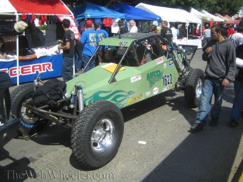 1990 Ford Bronco - green single-seat tube-chassis off-road race buggy numbered 1622 with flame graphics is parked among vendor tents.