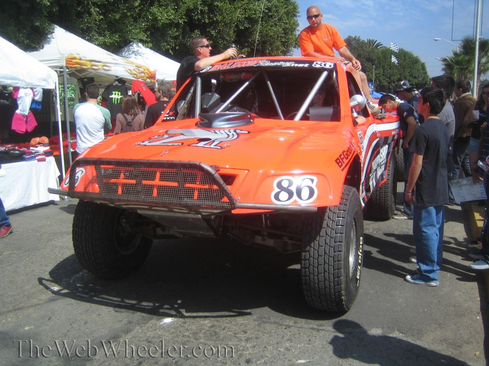 Orange off-road race truck No. 86 with two men seated atop in a crowd