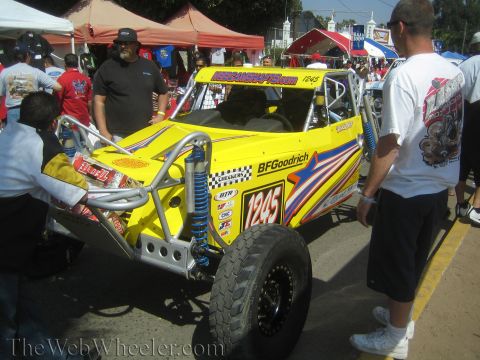 1990 Ford Bronco - yellow tube-chassis off-road race buggy numbered 1245 with star graphics and BFGoodrich branding is surrounded by people outdoors.