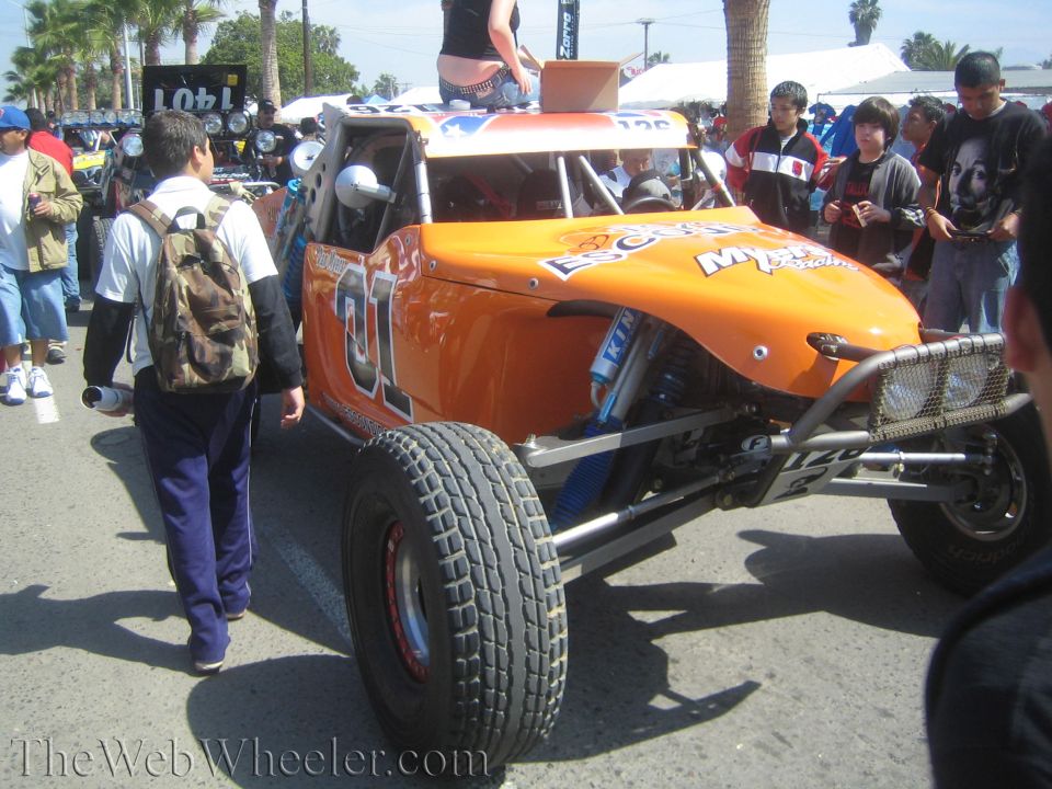 Orange off-road race buggy No. 01 with crowd walking past at outdoor event