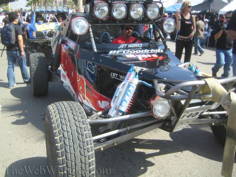 1990 Ford Bronco - dark off-road race buggy numbered 140 with a roof light bar, Jet Works and BFGoodrich graphics and a seated driver is surrounded by a crowd.