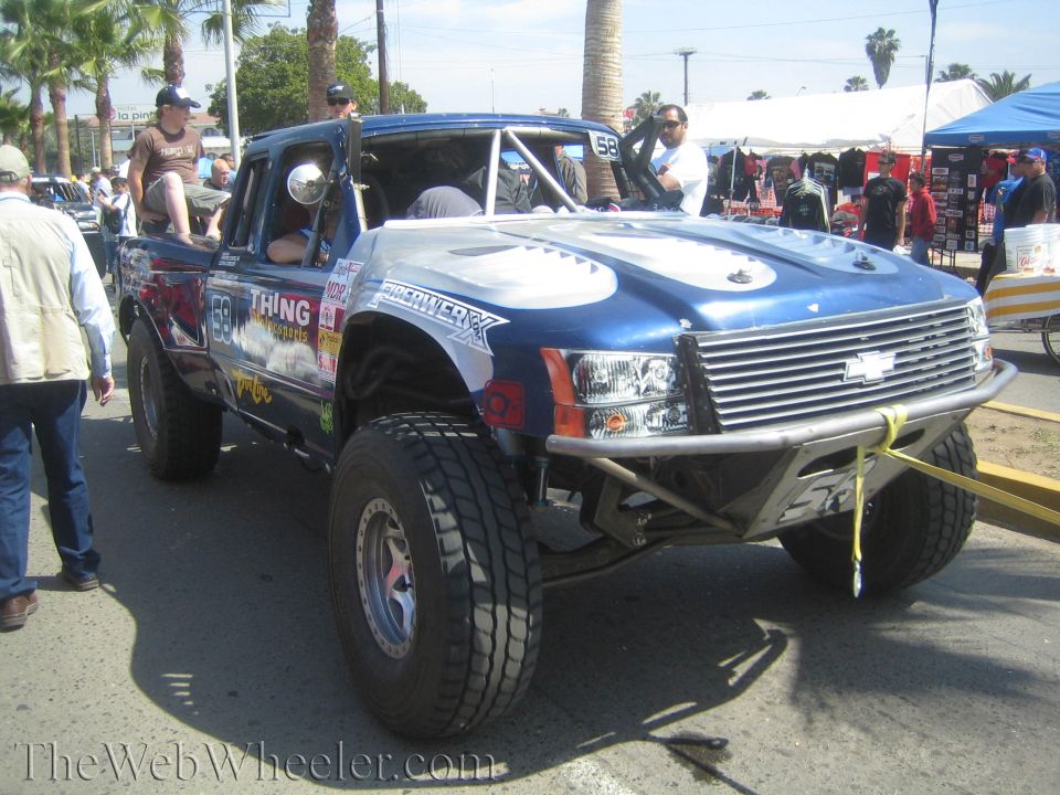Blue Chevrolet prerunner race truck No. 66 with crowd on sunny street