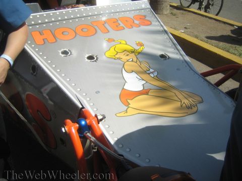 1990 Ford Bronco - silver riveted body panel on a race vehicle carries a HOOTERS pin-up girl decal and simulated bullet-hole stickers.