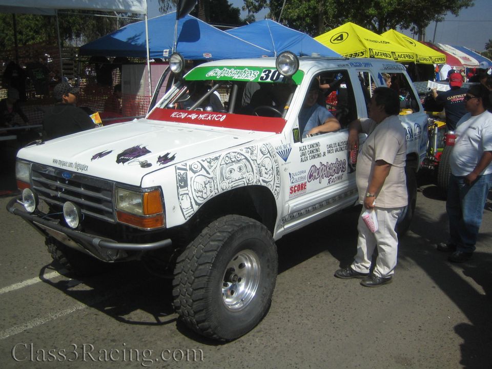 White lifted Ford race truck with intricate graphics at off-road event