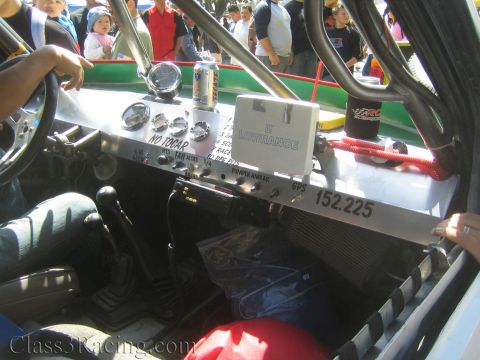 1990 Ford Bronco - aluminum dashboard of a race vehicle holds gauges, labeled switches, a Lowrance GPS unit and a soda can, with a driver at the wheel.