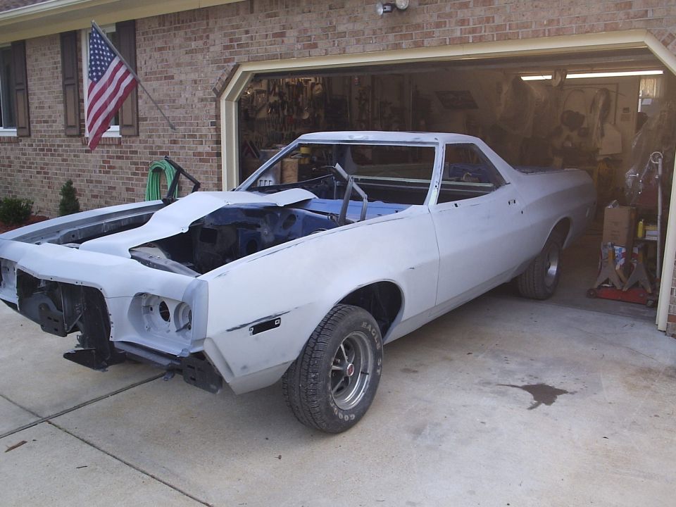 Primer gray Ford Ranchero mid-restoration, front-left view in driveway by garage