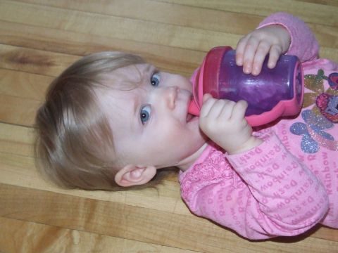 1990 Ford Bronco - A baby lies on a wooden floor, drinking from a sippy cup.