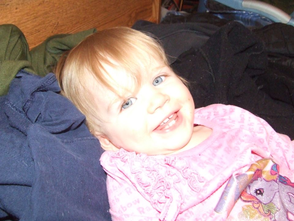 Baby girl with blonde hair and blue eyes smiling, wearing a pink shirt