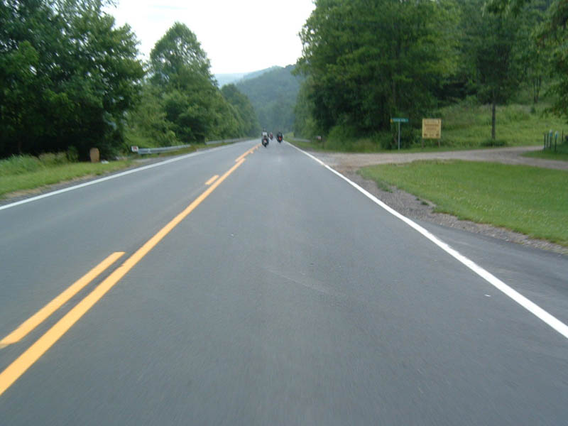 Motorcycles on a two-lane road with trees and hills in the background