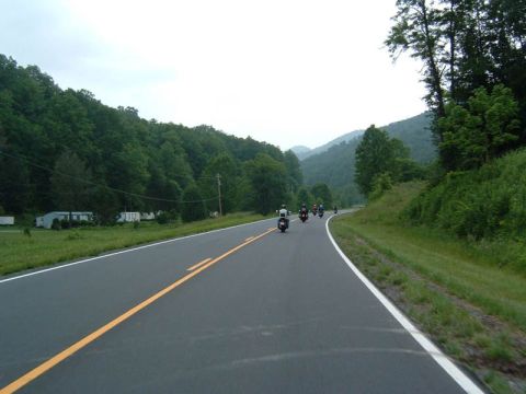 1985 Ford LTD Crown Victoria - A group of motorcyclists ride together on a scenic road surrounded by trees and mountains.
