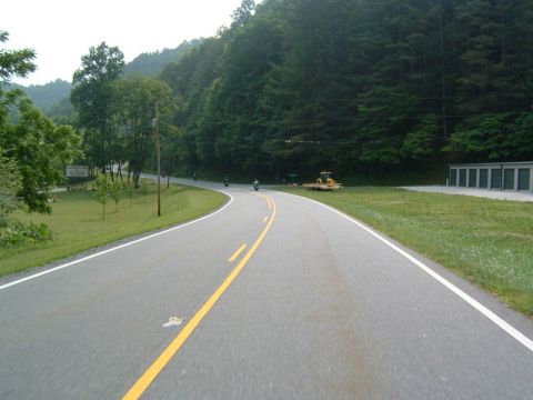 1985 Ford LTD Crown Victoria - Several motorcycles ride along a scenic, tree-lined road on a sunny day.