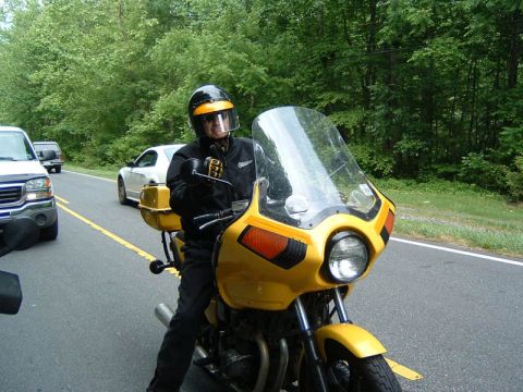 1985 Ford LTD Crown Victoria - A rider on a yellow motorcycle is on a road with other vehicles in the background.