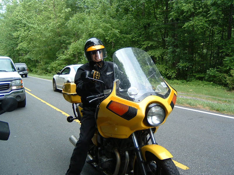 Yellow motorcycle with a rider wearing a black helmet and jacket, seen from the front on a road