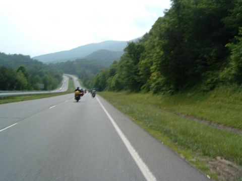 1985 Ford LTD Crown Victoria - Motorcycles travel down a highway surrounded by trees and mountains.
