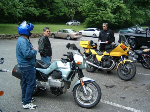 1985 Ford LTD Crown Victoria - A group of people gather around motorcycles in a parking lot on a cloudy day.