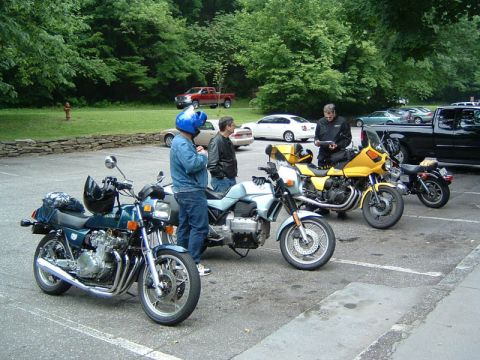 1985 Ford LTD Crown Victoria - Several motorcycles are parked in a lot, with people gathered near them.